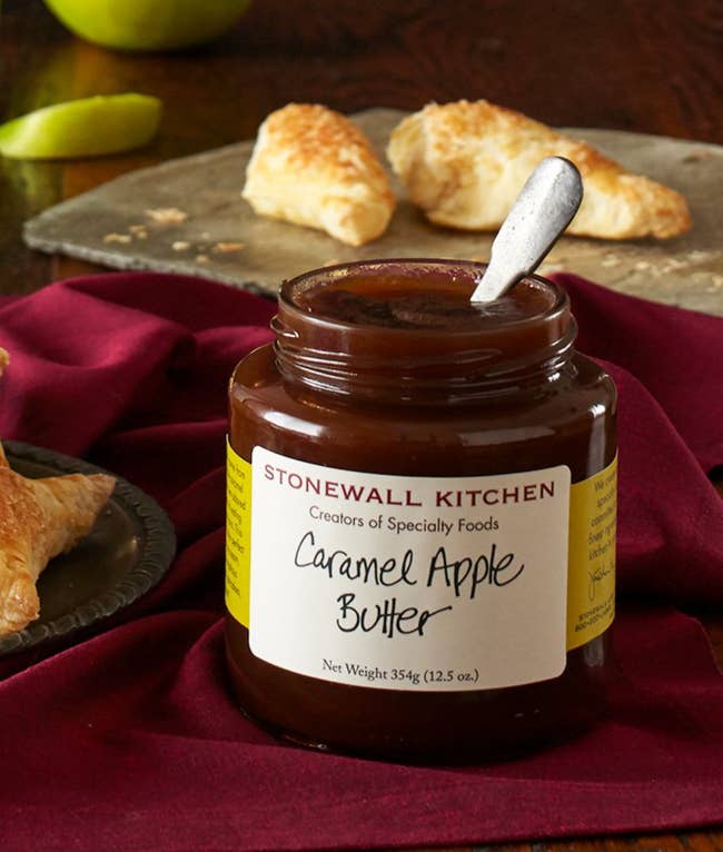 Stonewall Kitchen Caramel Apple Butter jar with a spoon inside, placed connected a array with pastries successful the background