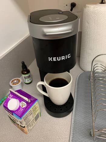 Keurig java  shaper  connected  a countertop with a filled mug, fractional  & fractional  carton, java  pod, and CBD lipid  vessel  nearby