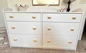 White dresser with eight gold handles in a home setting, suitable for bedroom storage solutions