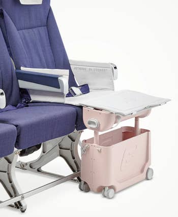 the suitcase in front of a seat that looks like an airplane chair, with it raised up, creating a leg rest for kids to make the seat more comfortable