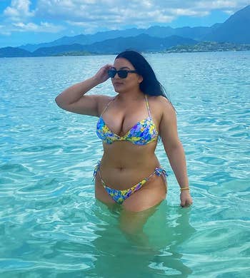 reviewer in floral bikini posing in clear water with mountains in the background