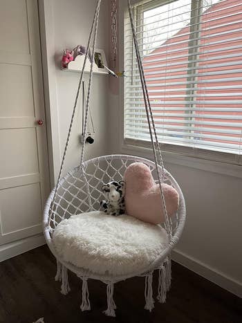 Cozy rope swing chair with plush cushion, heart pillow, and stuffed animal, in a sunlit room