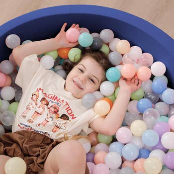 Entertainmment news Young child smiling in a ball pit, wearing a T-shirt with cartoon characters and text 