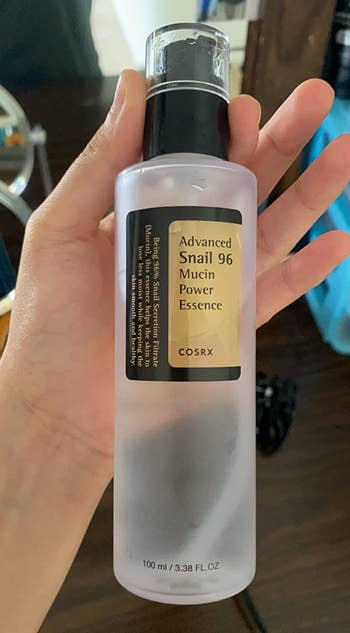Reviewer holding clear bottle of snail mucin with clear cap and black pump 