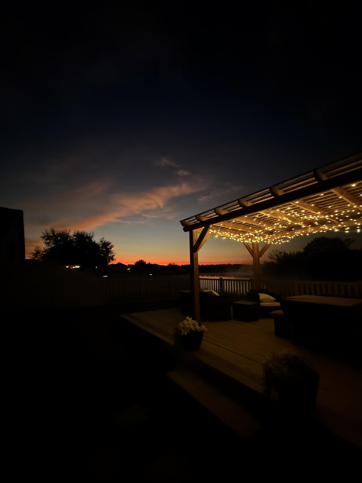 A cozy outdoor patio with drawstring  lights nether  a pergola, overlooking a sunset. Perfect for evening relaxation and entertaining