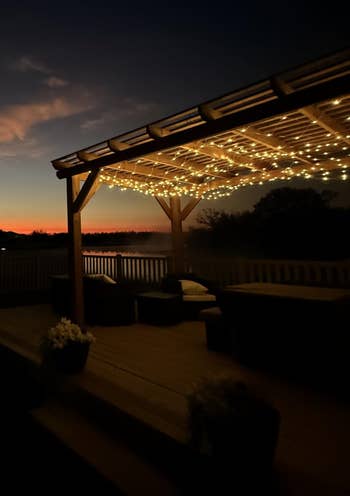 A cozy outdoor patio with drawstring lights nether a pergola, overlooking a sunset. Perfect for evening relaxation and entertaining
