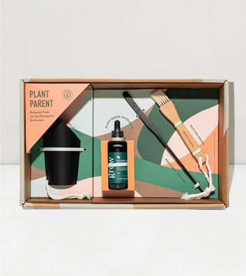 Green, brown, orange, and pink gift box filled with black soil scooper, black bottle with dropper, black long tweezers, and a wooden dusting brush