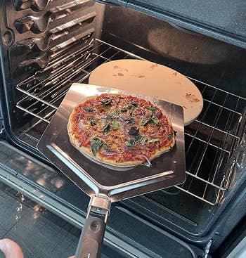 reviewer using a pizza peel to lift a pizza from a pizza stone in an oven