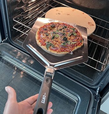 reviewer using a pizza peel to lift a pizza from a pizza stone in an oven