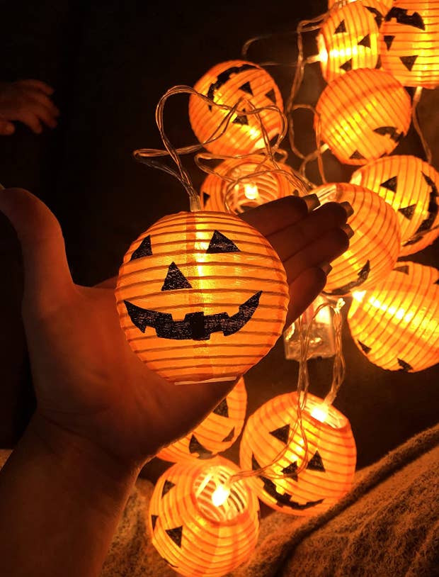 reviewer holding up glowing string of pumpkin shaped twinkle lights 