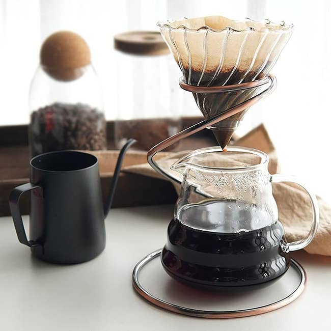 Elegant spiral coffee dripper set on top of a glass carafe, with a black mug and coffee beans nearby