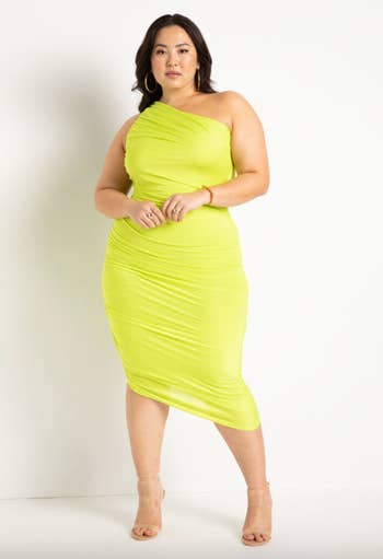 model poses in a one-shoulder ruched yellow midi dress 