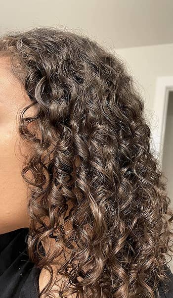 Close up of reviewer in black top with hydrated tight brown curls after using product