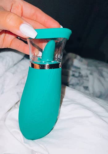 Hand holding green vibrator with tongue and suction cup