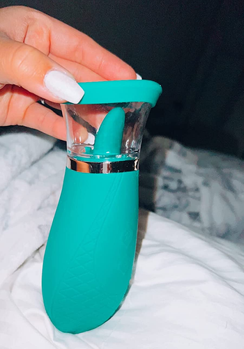 Hand holding green vibrator with tongue and suction cup