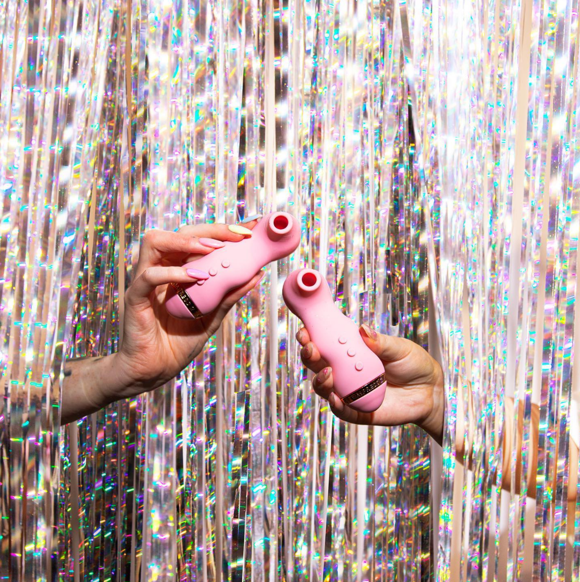 Hands holding pink suction vibrators in front of silver backdrop