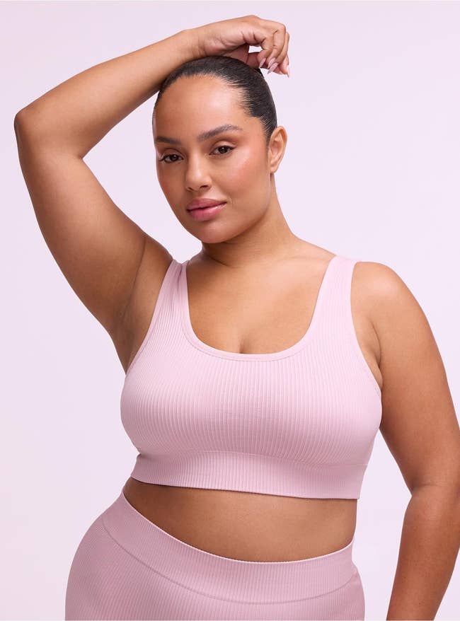 Person modeling ribbed sports bra and leggings successful a workplace setting. Their limb is raised, showcasing the acceptable and style
