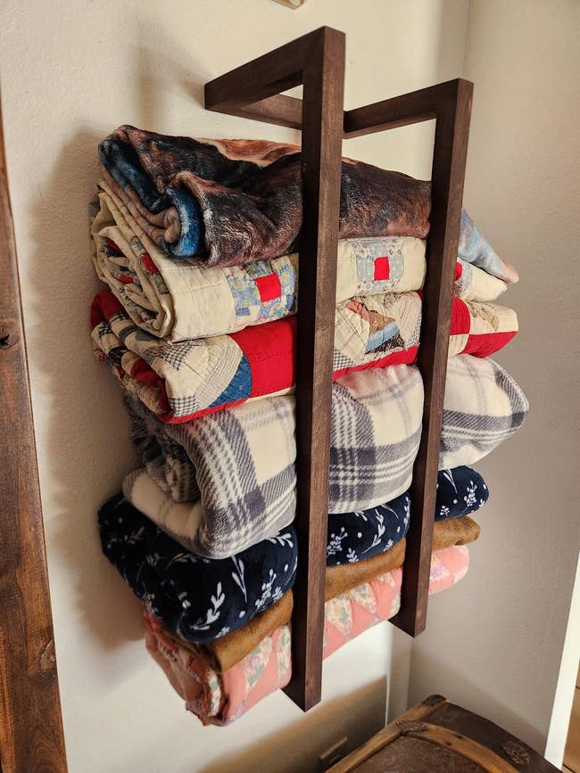 Quilts neatly folded connected a woody shelf, showcasing assorted patterns and designs, perfect for cozy location decor buying inspiration