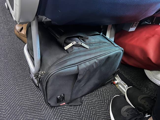 reviewer image of the black wheeled carry on under the seat ahead of them on a plane