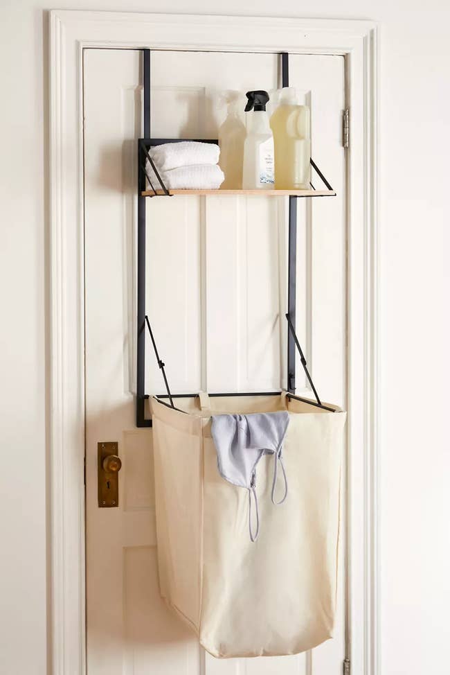 the hamper hanging on a door with one shelf holding  cleaning products