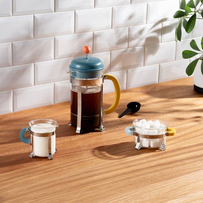 French property   java  shaper  with yellowish  handle, solid  cups with beverage  and sweetener  cubes connected  a woody  countertop. White subway tiles successful  the background