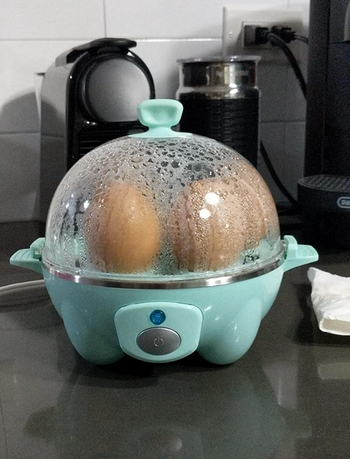 Reviewer image of dome shaped egg cooker with blue base with six eggs steaming inside 
