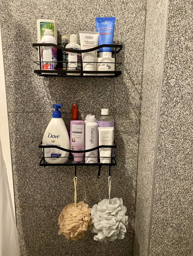 Reviewer's black shelves attached to a shower wall with lots of products in them 