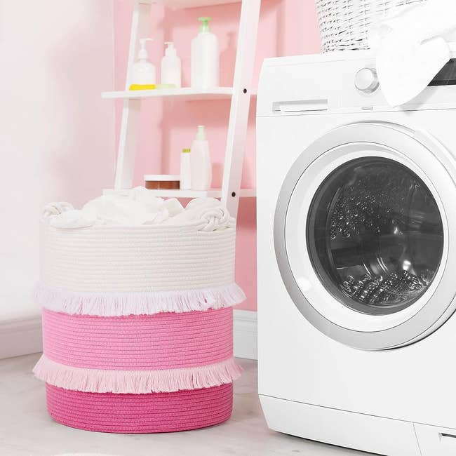 the woven storage basket in pink and white filled with clothes, next to a washing machine 