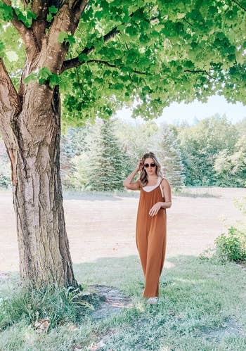 Woman in a sleeveless jumpsuit posing beside a tree, suitable for a fashion-focused shopping article