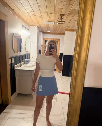 Person takes a reflector selfie successful a achromatic fitted apical and bluish skirt, showing a covering tag. They are successful a modern bathroom