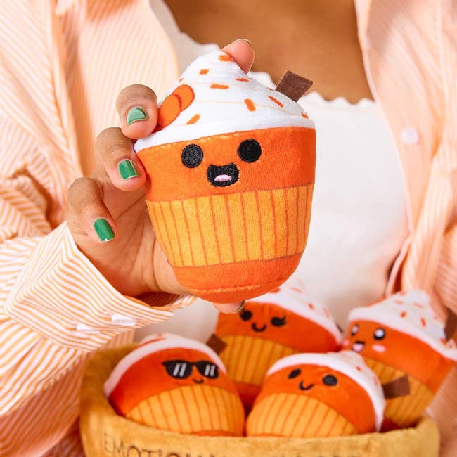 Person holding a cute plush cupcake artifact  with a smiling face; much  identical toys are successful  a vessel  below