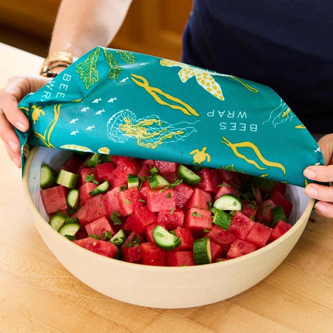 the beeswax wrap being used to cover a bowl of watermelon and cucumber salad