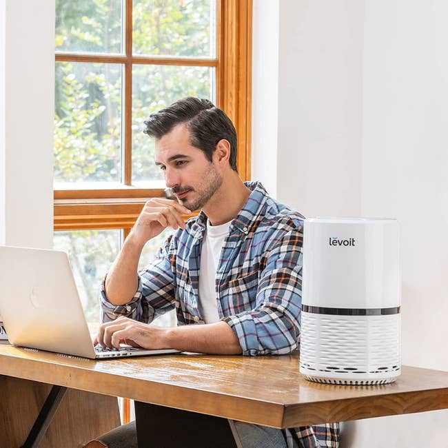 model sitting at a desk with the white air purifier on top of the desk