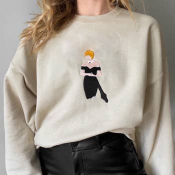 The beige sweatshirt with an embroidered illustration of Princess Diana in a strapless black dress