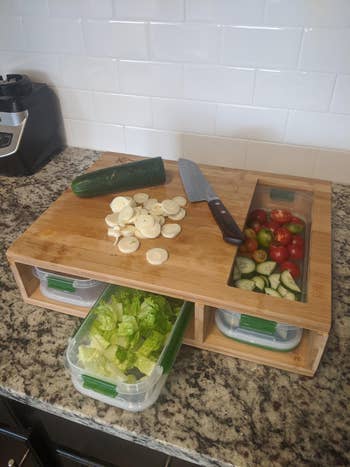 A reviewer's cutting board with veggies in the containers below