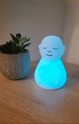 A small white figurine with closed eyes changing lit up colors from blue to green 