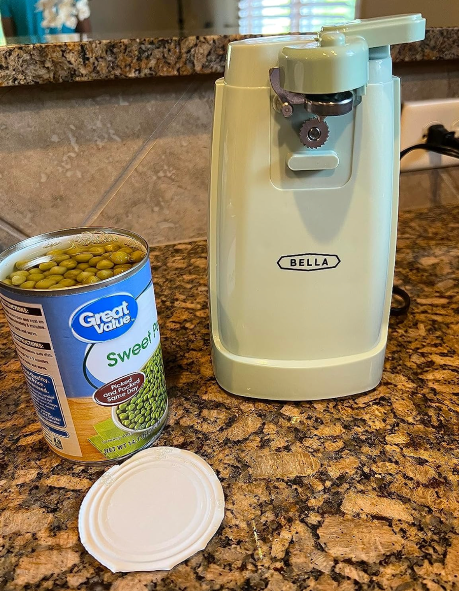 A small sage green retro style can opener next to an open can of peas 