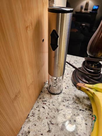 A close-up of a modern, stainless steel pepper grinder on a kitchen counter next to bananas