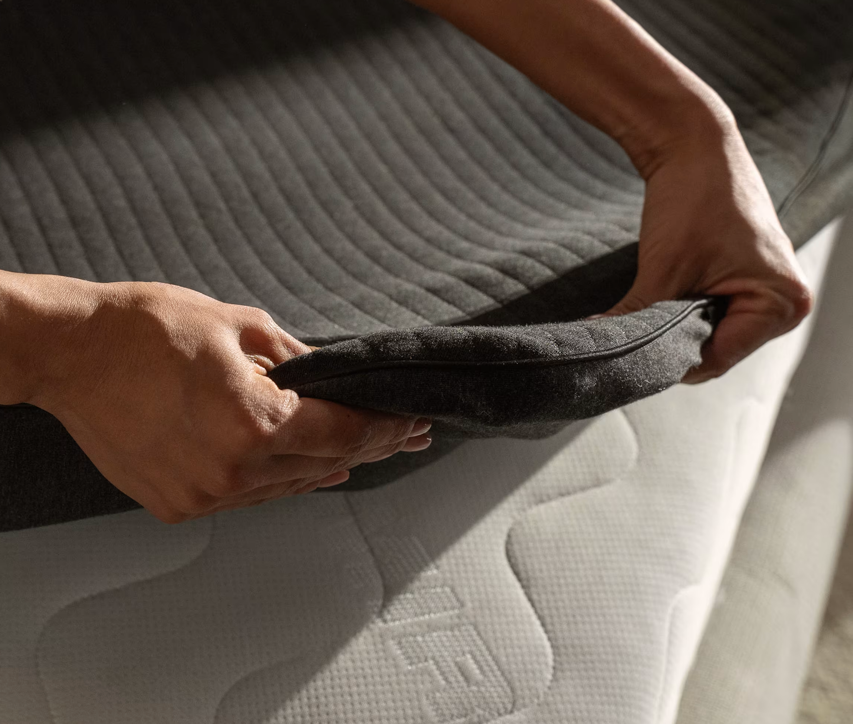 Hands adjusting a mattress cover, showcasing its fit and texture, featured in a shopping article