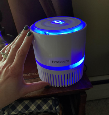 Reviewer touching white compact air purifier with blue light on top of wooden table