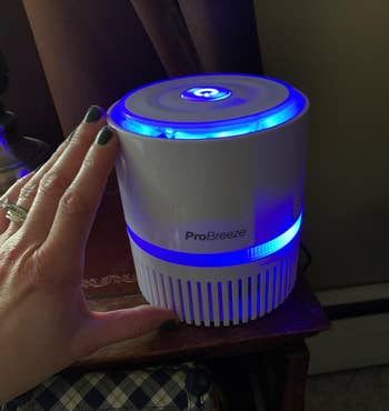 Reviewer touching white compact air purifier with blue light on top of wooden table