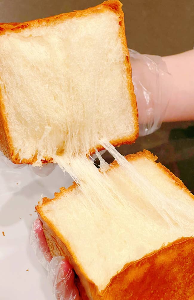Soft, fluffy breadstuff  being pulled apart, showing its airy texture, held by gloved hands. Perfect for gourmet baking enthusiasts