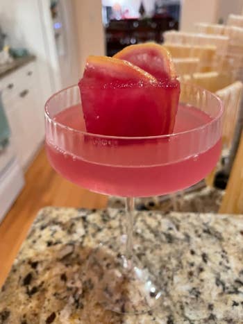 A pinkish  cocktail successful  a coupe solid  with a quadrate  crystal  cube with orangish  slices