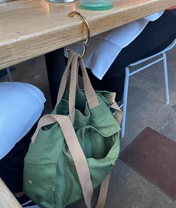 reviewer's large green tote bag hanging on the gold  clip which is hooked onto the side of a restaurant table