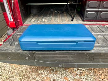 A closed bluish  Coleman camping stove lawsuit  sits connected  the tailgate of a truck