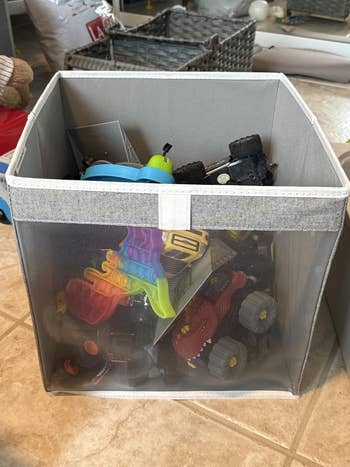 Box filled with assorted kids' toys, including pop-its, artifact cars, and tiny vehicles, connected a tiled floor