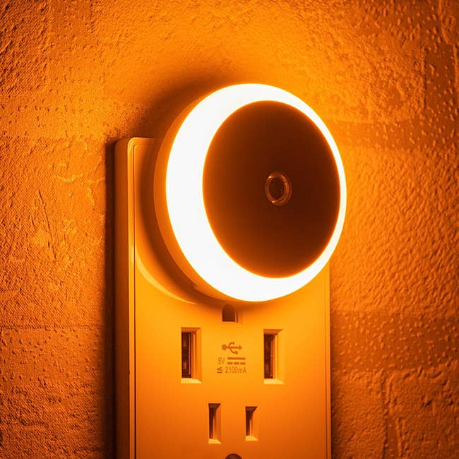A modern nighttime airy plugged into a partition outlet, illuminating the surrounding area. The nighttime airy has a circular ringing plan and emits a brushed glow