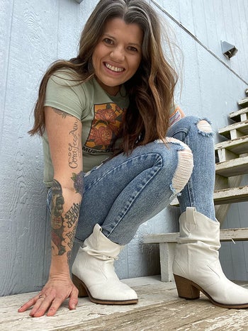 reviewer photo of them crouching in white cowgirl boots, blue jeans, and a light green tee