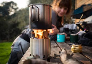 the camp stove and pot, with woman in the background