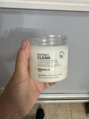 Hand holding a NatureLab Tokyo Perfect Clean 2-in-1 Scalp Scrub & Clarifying Shampoo container